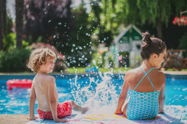 İki çocuk havuz kenarında suyu sıçratarak eğleniyorlar.