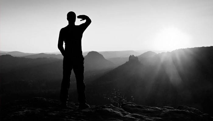 Dağların üzerinden doğan güneşe bakan genç erkek. Resim siyah beyaz